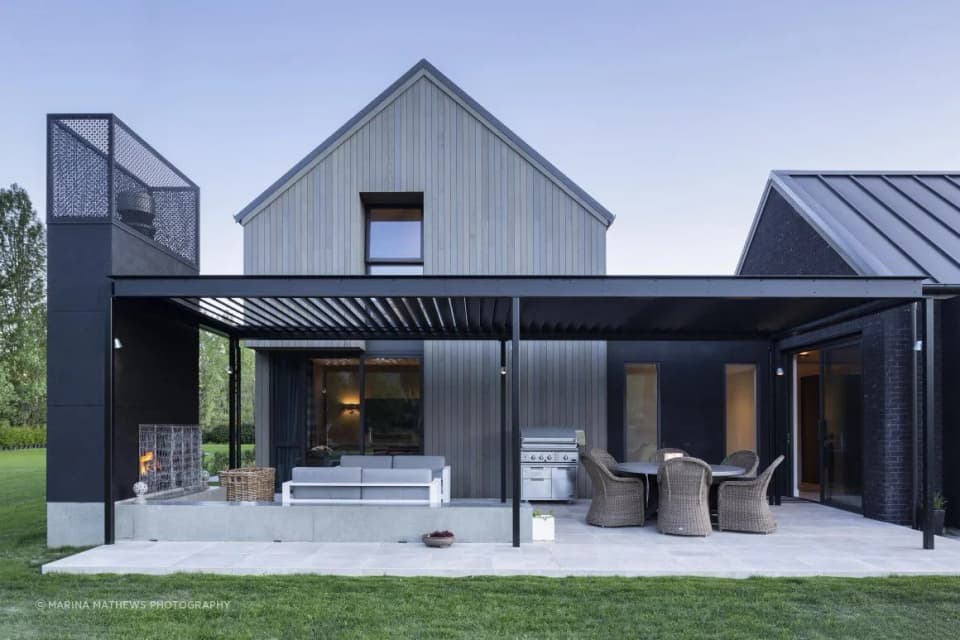 Black steel pergola over a terrace on a timber-clad house