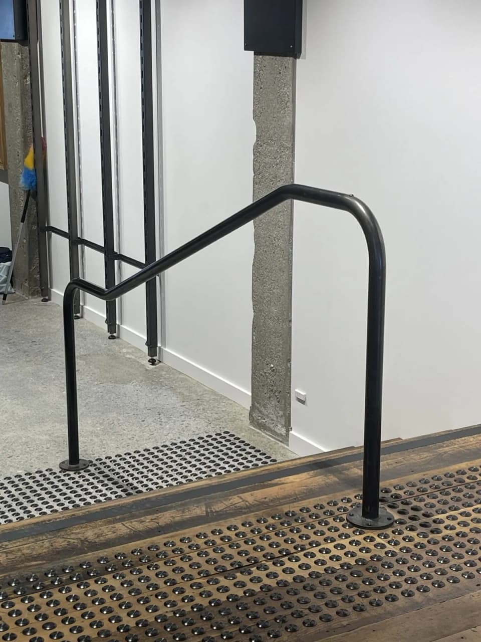 Black steel tubular handrail on a concrete stair in a commercial fit-out, with a returned end and floor-fixed post