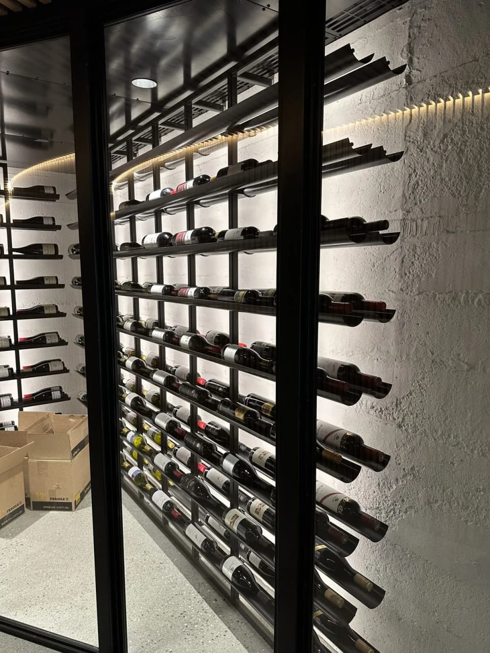 Black steel wine wall with bottles stored on laser-cut pin racks against a stone wall
