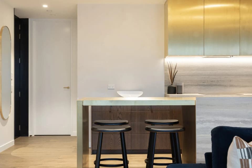 Brass canopy over a kitchen island with two bar stools, seen from the living room