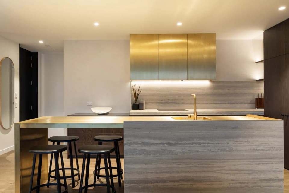 Brushed brass-clad kitchen canopy above a stone island with brass tapware