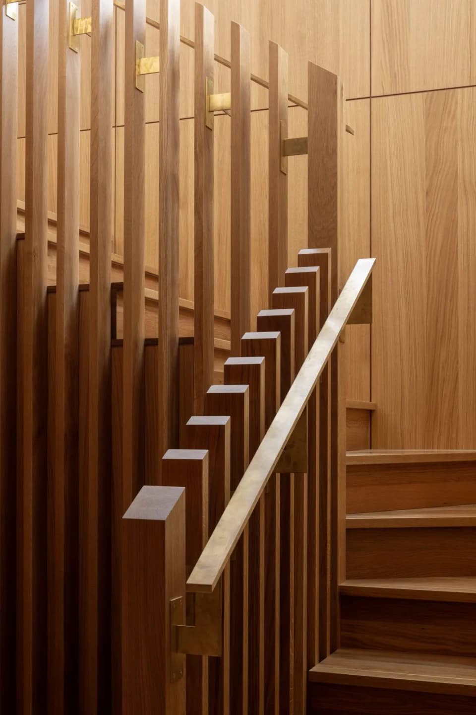 Slim brass handrail running up a timber batten staircase