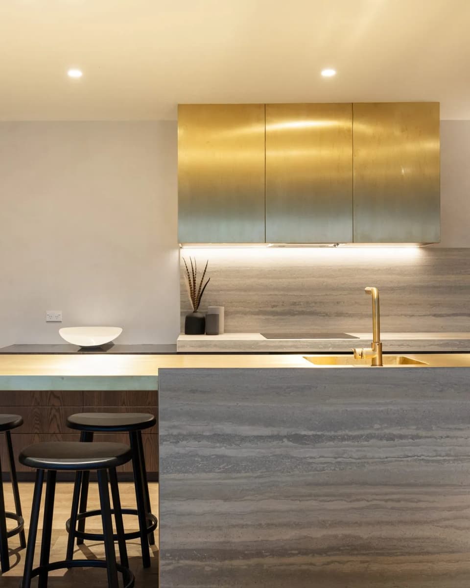 Brass overhead cabinets above a stone bench, with a brass tap