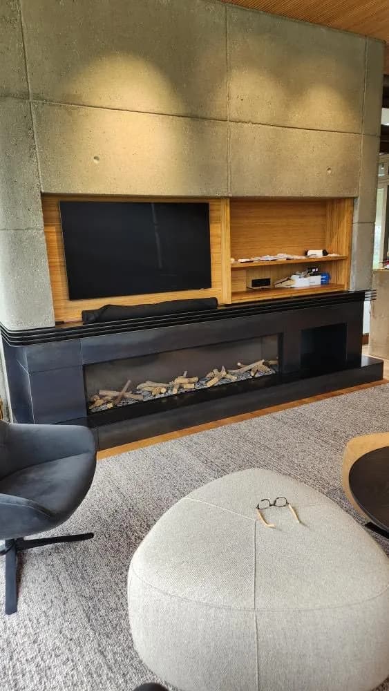 Blackened steel linear fireplace surround running under timber shelving and a wall-mounted TV