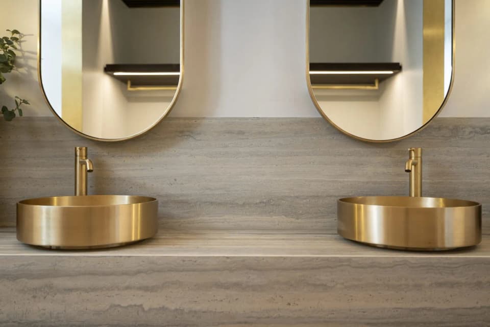 Double brass vessel basins and round brass mirrors on a travertine vanity