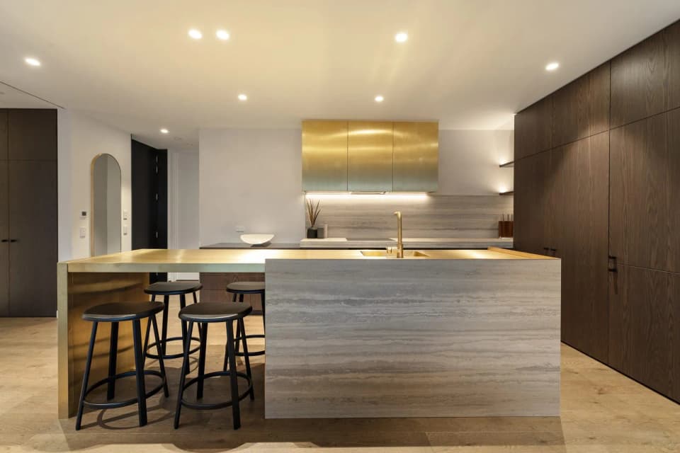 Open-plan kitchen with a brass-clad canopy, stone island and bar stools