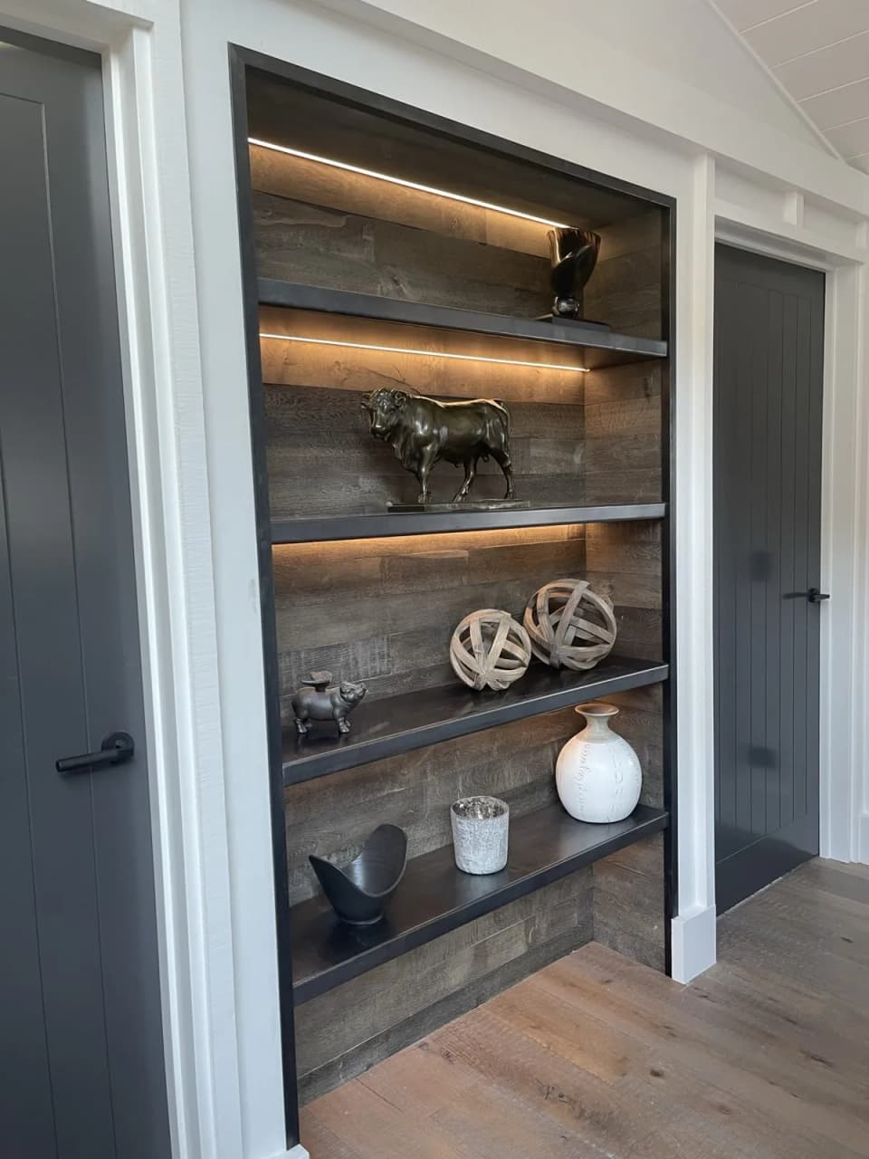 Blackened steel shelving niche with integrated lighting, built into a wall