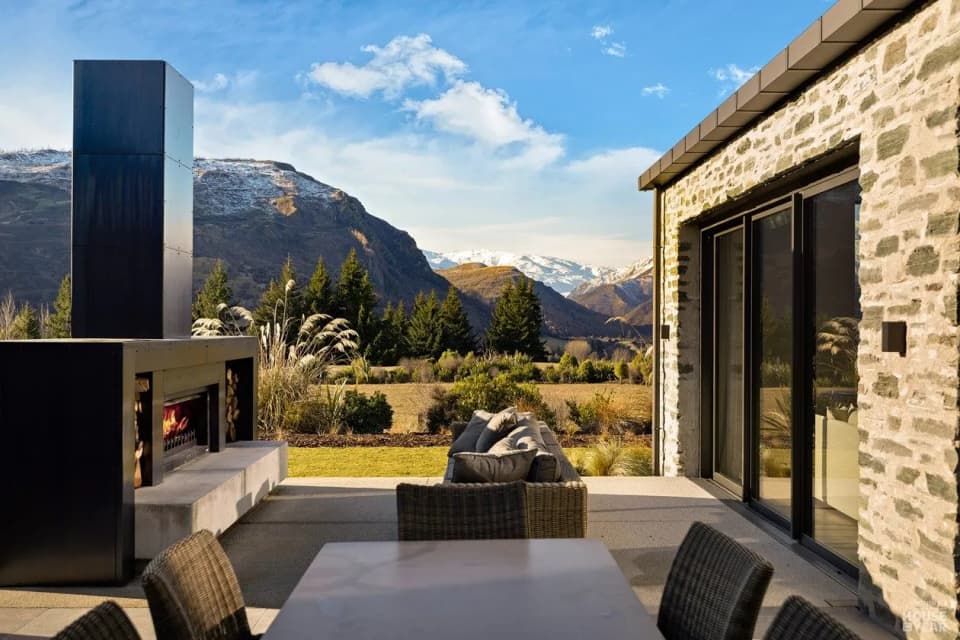 Built-in outdoor fireplace with a tall black steel chimney, mountains behind