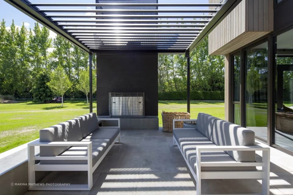 Covered outdoor pavilion with a dark steel fireplace wall and outdoor lounge seating, Speargrass Flat