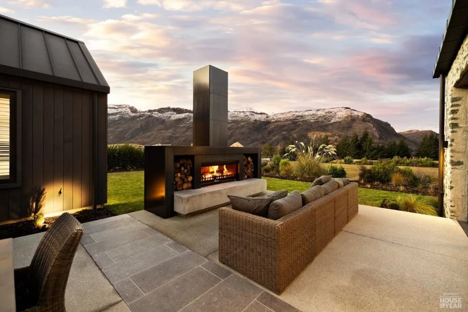 Outdoor fireplace with a steel chimney on a covered terrace at dusk, looking across the Wakatipu Basin