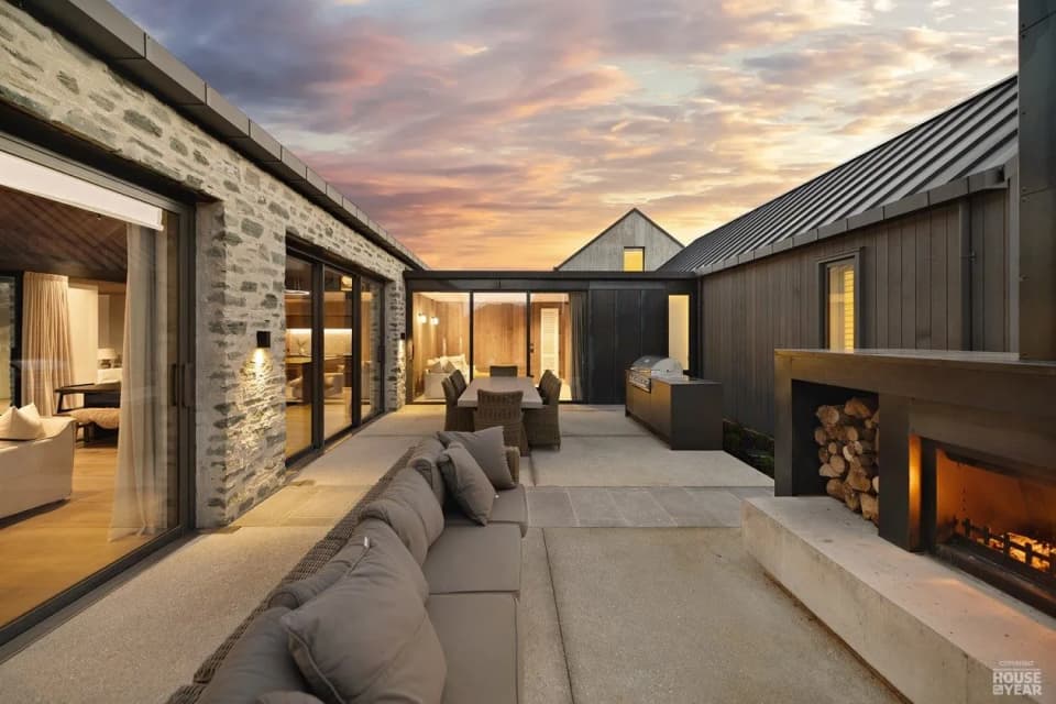 Outdoor living area with a built-in steel fireplace between a stone wall and a sunken lounge