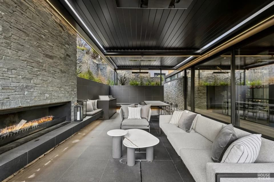 Covered outdoor lounge with a linear steel fire set into a stone wall
