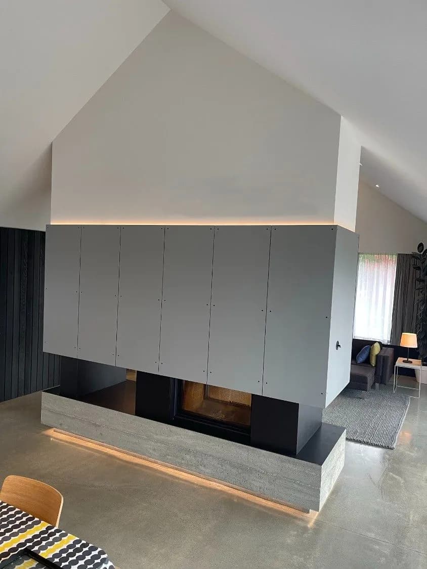 Double-sided fireplace clad in grey folded steel panels, dividing a living room from the dining space