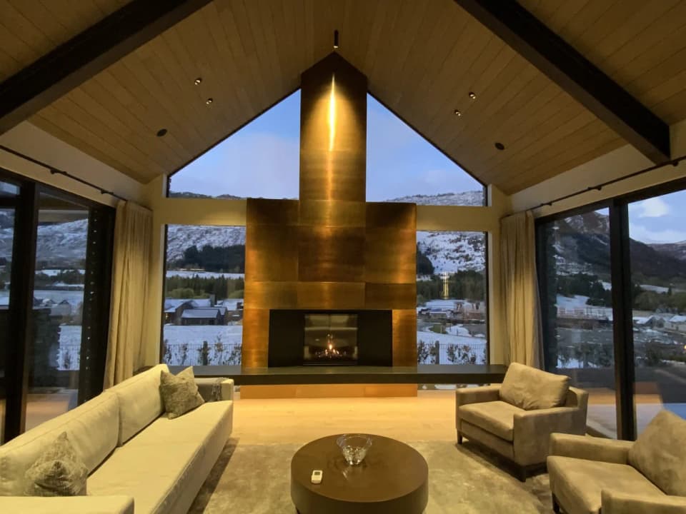 Patinated metal-clad fireplace and chimney rising to the ridge of a gable living room, with mountain views either side