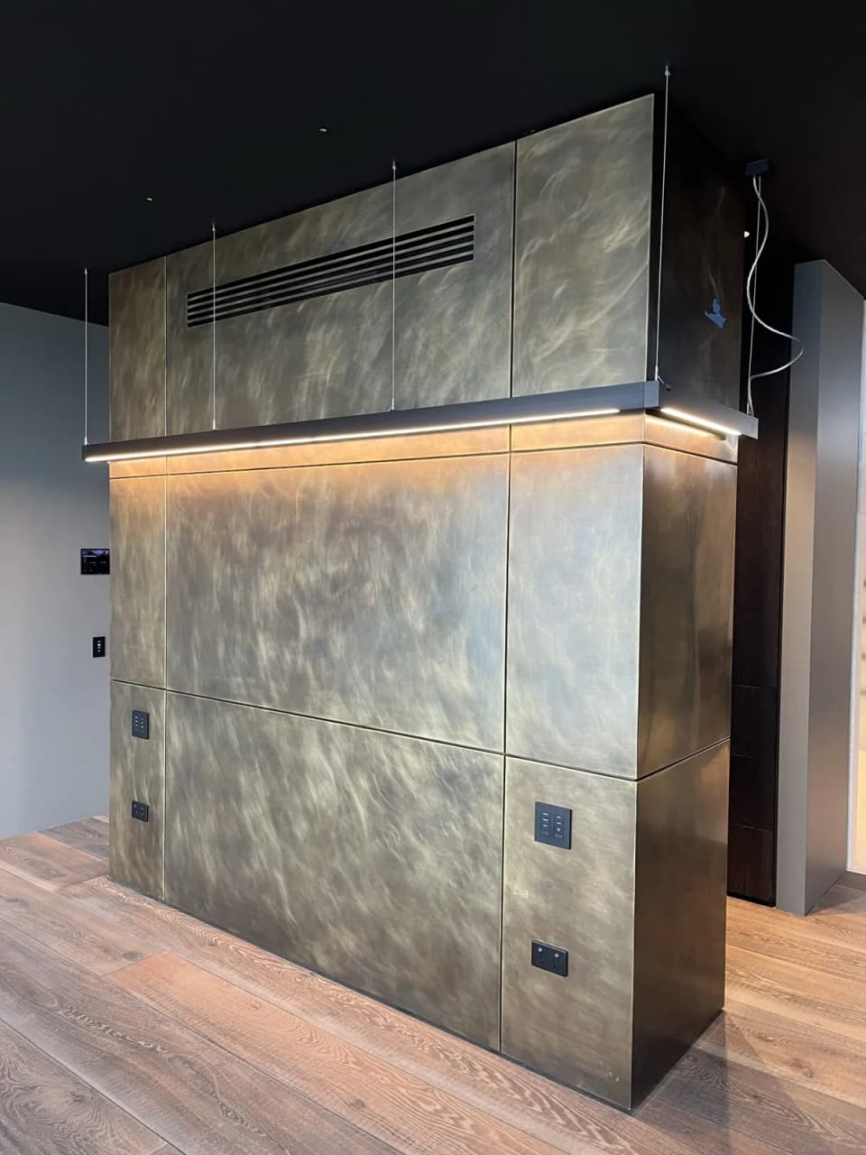 Patinated brass cladding on a tall joinery unit, with an LED strip under the overhead cabinet