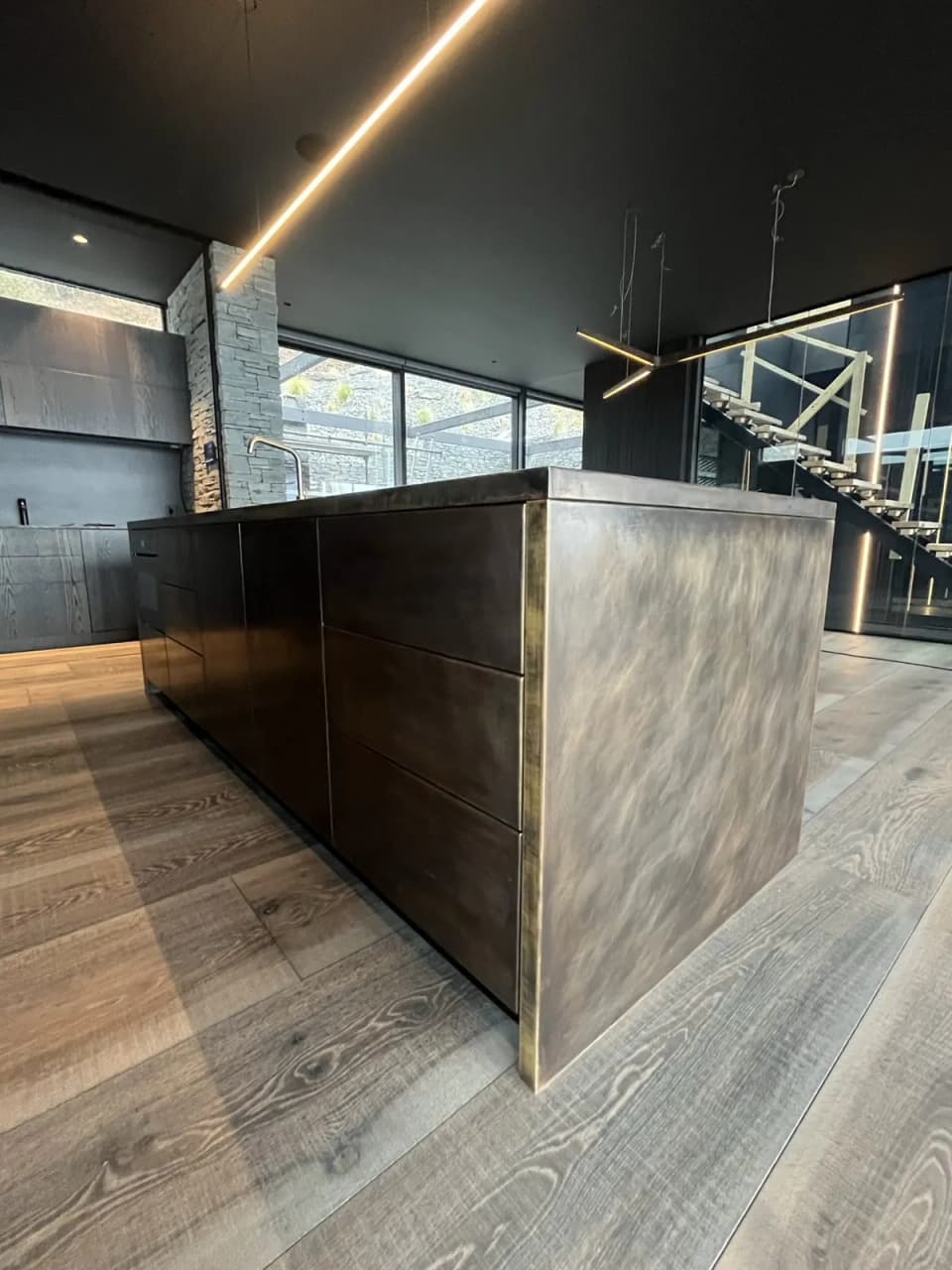 Kitchen island clad in patinated brass with a mottled dark bronze finish, in an open-plan living space