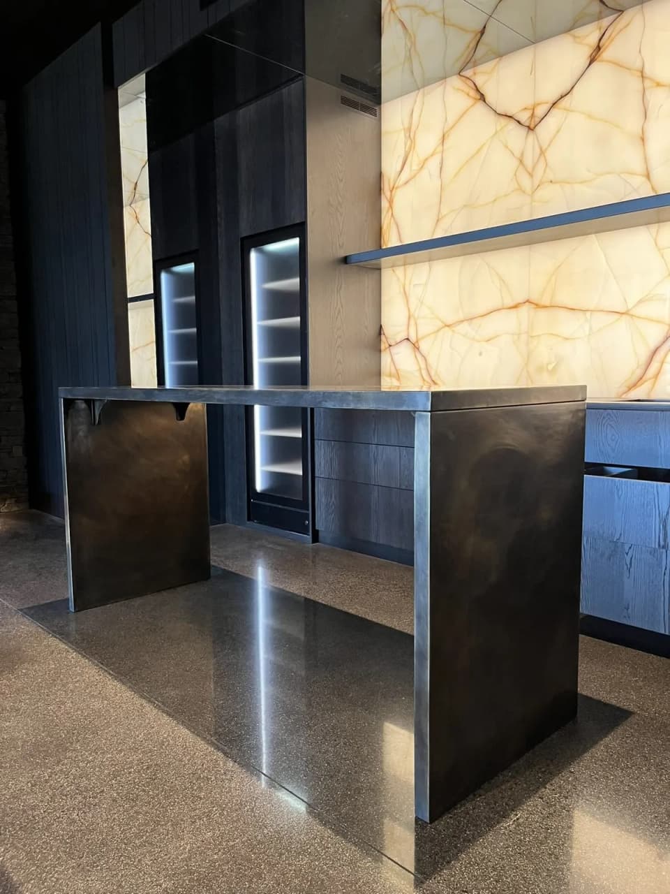 Patinated brass-clad island against a backlit onyx wall