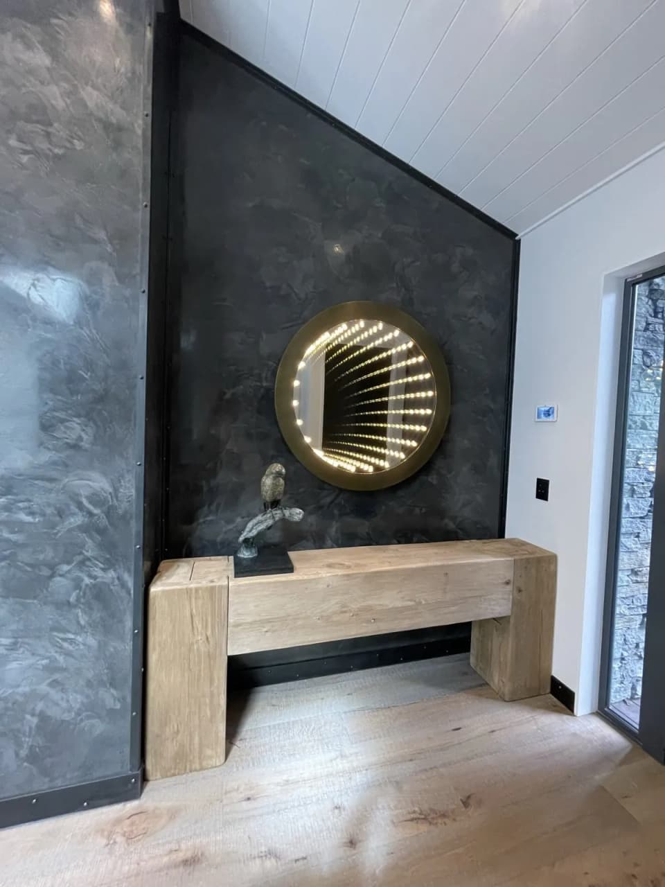 Round brass-framed mirror mounted on a patinated steel feature wall