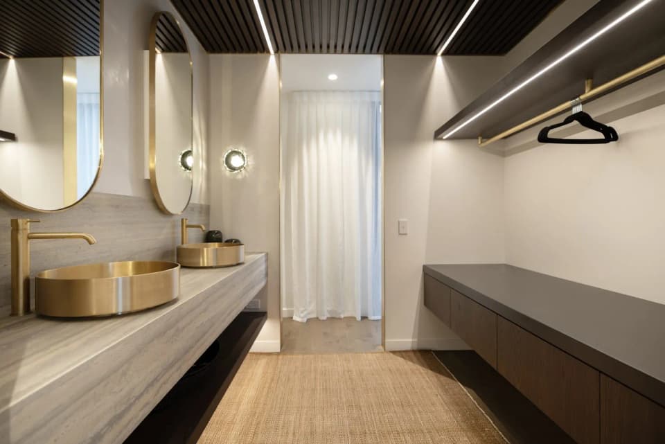 Round brass-framed mirror and brass basin in an ensuite with a stone vanity