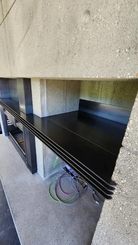 Close-up of a blackened steel hearth and fireplace lintel set flush into a board-formed concrete wall