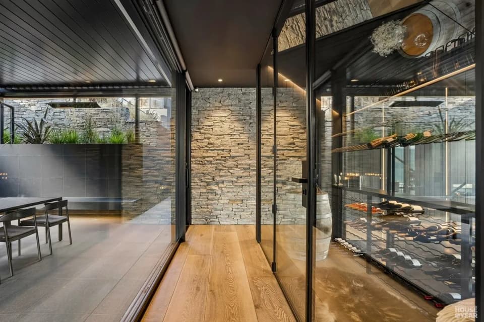 Steel-framed glazed wine room with black racking beside a schist wall