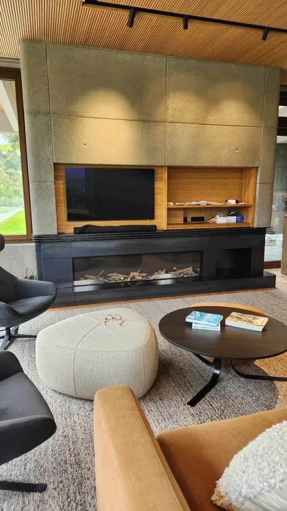 Dark steel linear fireplace set into a timber-lined living room wall, with the firebox and hearth plate in blackened steel
