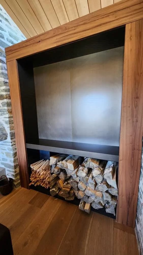 Steel-lined wood store niche built into a schist wall beside a dark steel fireplace