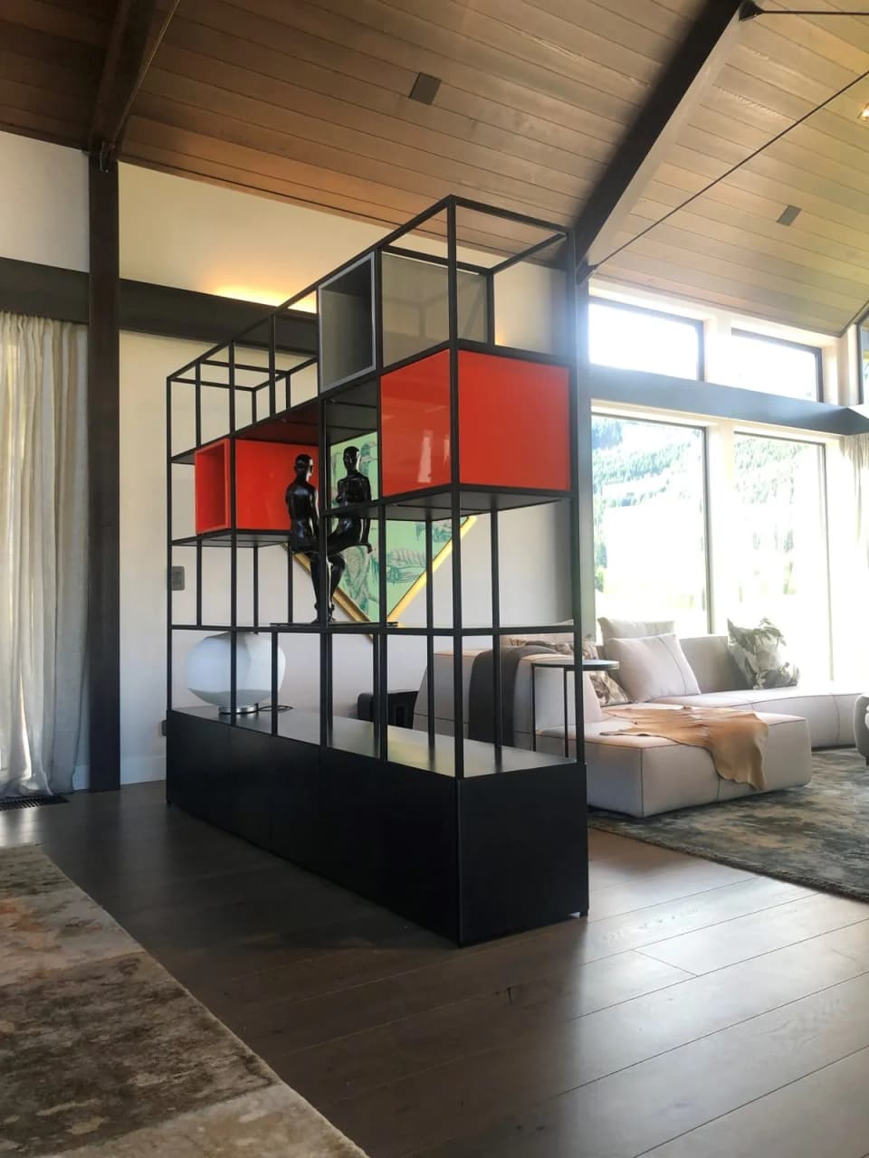 Floor-to-ceiling black steel screen with open shelving and coloured boxes, dividing a living space